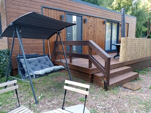 A wooden deck with a swing chair and a bench, leading to a modern building with large windows.