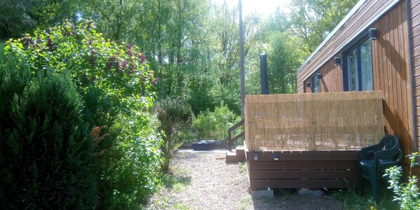 A wooden cabin with a covered deck, surrounded by dense greenery and trees.