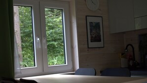 A room with a wooden interior, a window with a view of greenery, a clock on the wall, and a framed picture. - Tiny house in unspoiled nature on Lake Plau (Bad Stuer)