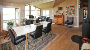 Een ruime woonkamer met een grote houten eettafel, zwarte stoelen, een bank en een open haard.