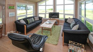 Een gezellige woonkamer met twee banken, een salontafel en een televisie. Grote ramen bieden uitzicht op het omliggende landschap.