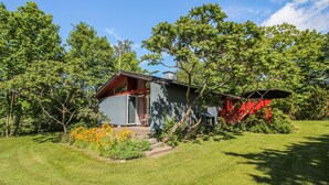 Ein kleines, eingeschossiges Haus mit geneigtem Dach, umgeben von üppigem Grün und Bäumen.