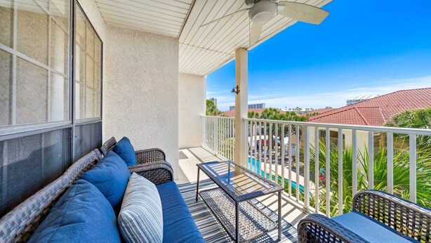 Een balkon met rieten meubilair, uitzicht op het zwembad en een heldere lucht.