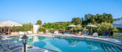 A swimming pool with lounge chairs and umbrellas, surrounded by greenery.