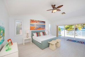 Une chambre spacieuse avec un grand lit, un ventilateur de plafond et une vue sur l’océan, visible à travers la porte-fenêtre coulissante.