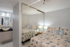 A bedroom with two beds, a large mirror, a bedside table with a lamp, and a bathroom with a sink and mirror. - 3870 Sand Castle - Ocean Front, Pools, Hot Tubs (Monterey)