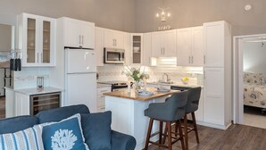 Une cuisine moderne avec des meubles blancs, un îlot central doté de tabourets et un lustre.