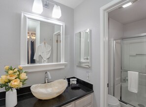 A bathroom with a large mirror, a sink with a beige basin, a vase with flowers, and a shower area. - 3870 Sand Castle - Ocean Front, Pools, Hot Tubs (Monterey)
