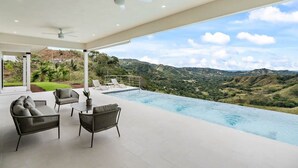 Un espacio lounge moderno al aire libre con piscina y vistas a un paisaje montañoso.