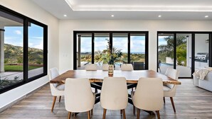 Un comedor moderno con una mesa grande y sillas, ventanas amplias que ofrecen vistas al exterior y un ventilador de techo.