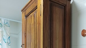 Een houten garderobe met twee deuren en een lade, in een badkamer met witte betegelde wanden en een douchegordijn met bladmotieven.