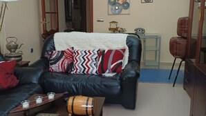 Een woonkamer met een zwarte leren bank, een houten salontafel en een kroonluchter.