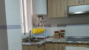 Een keuken met houten kastjes, een roestvrijstalen spoelbak, een witte kookplaat en een prullenbak.