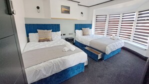 A modern hotel room with two beds, a ceiling light fixture, a small table, and a window with blinds. - Family Stay | Home from Home | Hot-Tub | Pets Free (BISPHAM)