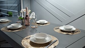 A modern dining area with a long table set for a meal, featuring woven placemats, white plates, and a bottle of champagne. - Family Stay | Home from Home | Hot-Tub | Pets Free (BISPHAM)