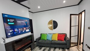 A modern living room with a flat-screen TV mounted on the wall, a gray sofa with colorful cushions, a fireplace with logs, and a patterned floor. - Family Stay | Home from Home | Hot-Tub | Pets Free (BISPHAM)