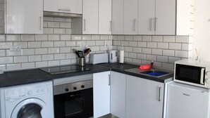 A compact kitchen with white cabinets, a washing machine, a microwave, and a sink.