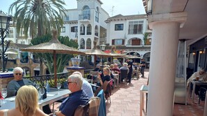 An outdoor café with tables and chairs, surrounded by buildings and palm trees.