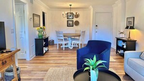 A living room with a TV, a blue armchair, a sofa, a dining area with a table and chairs, and a chandelier. - Spacious Villa, Near Shops & Beach in Harbour Town (Hilton Head Island)