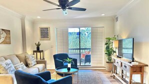 A living room with a sofa, chairs, a coffee table, a TV, and a balcony with a view. - Spacious Villa, Near Shops & Beach in Harbour Town (Hilton Head Island)