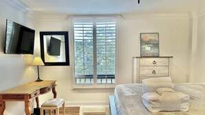 A bedroom with a bed, a desk, a chair, a window with blinds, a TV mounted on the wall, and a dresser. - Spacious Villa, Near Shops & Beach in Harbour Town (Hilton Head Island)