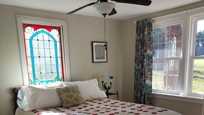 Un dormitorio con una cama grande, ventilador de techo, ventana de vitral y vista al exterior.