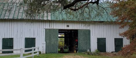 A white barn with green shutters, a wooden fence, and a gravel path leading to the entrance.