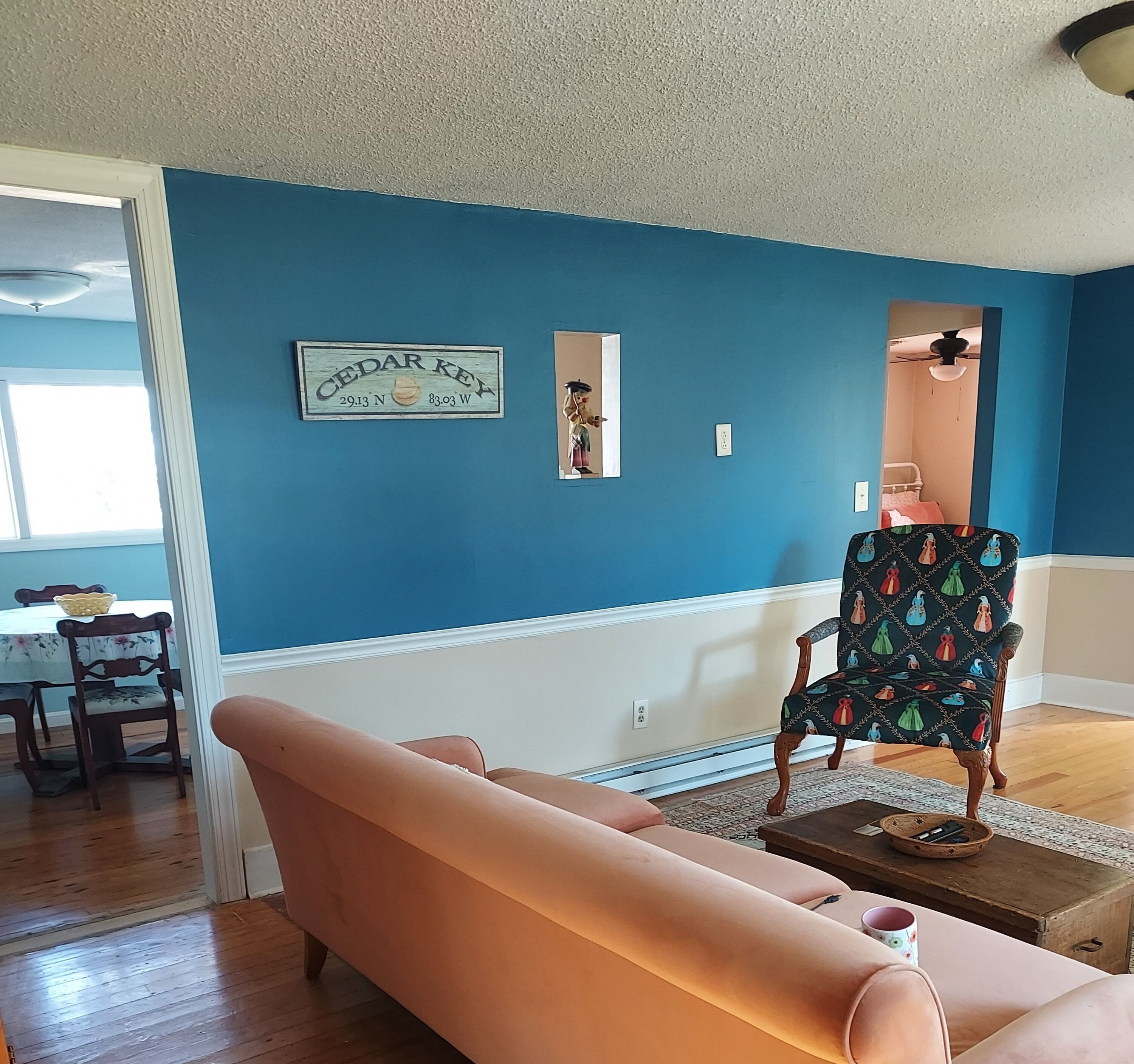 Uma sala de estar com parede azul, sofá rosa, poltrona estampada e uma pequena mesa com uma caneca.