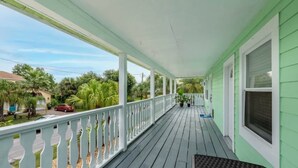 Une véranda couverte avec des balustrades blanches, une façade verte et une vue sur le quartier.