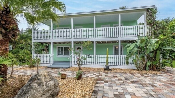 Un bâtiment à deux étages doté d’un balcon blanc et d’une terrasse en pierre à motifs géométriques.