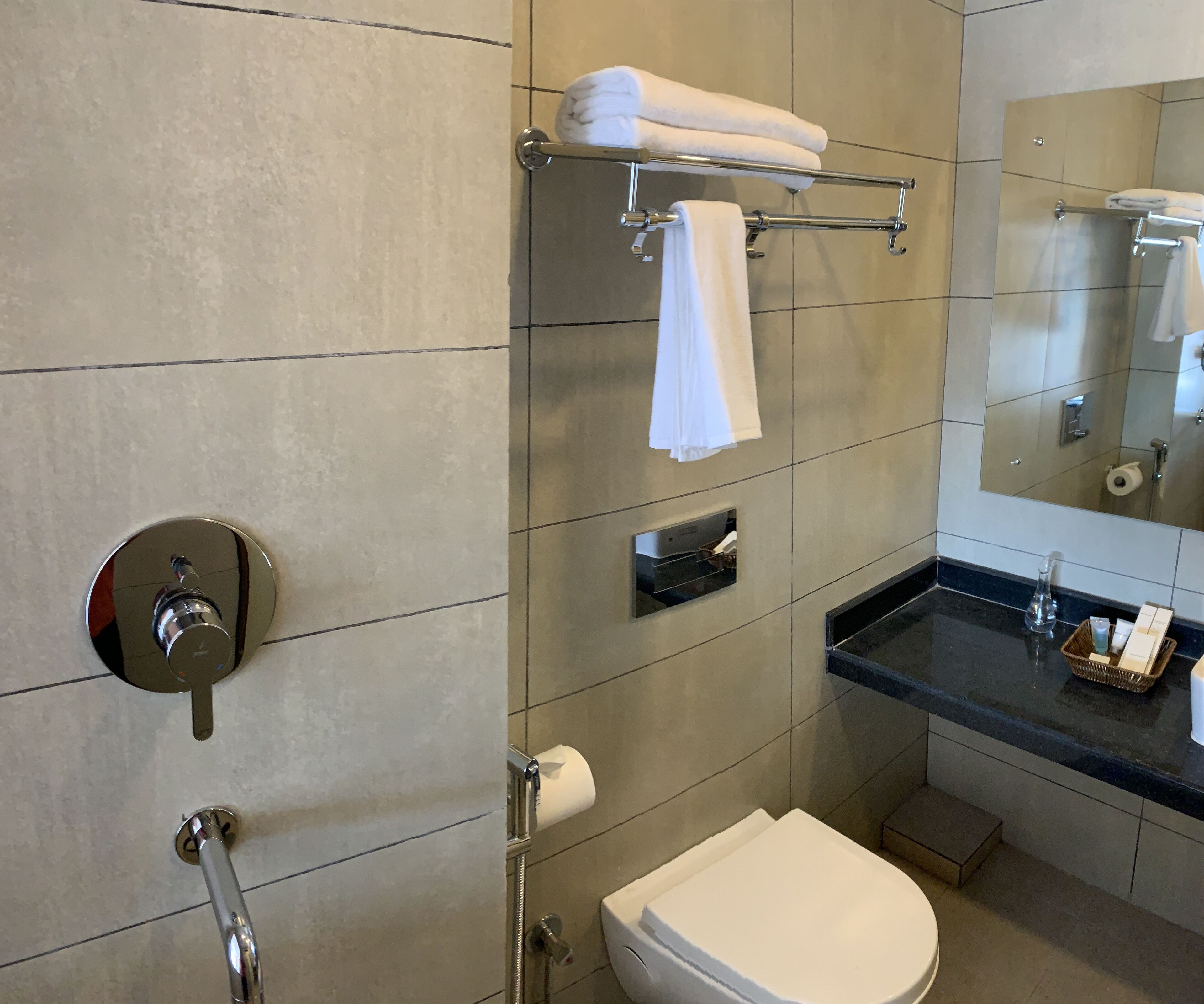 A modern bathroom with a toilet, a towel rack with towels, a hand dryer, and a small basket of toiletries.
