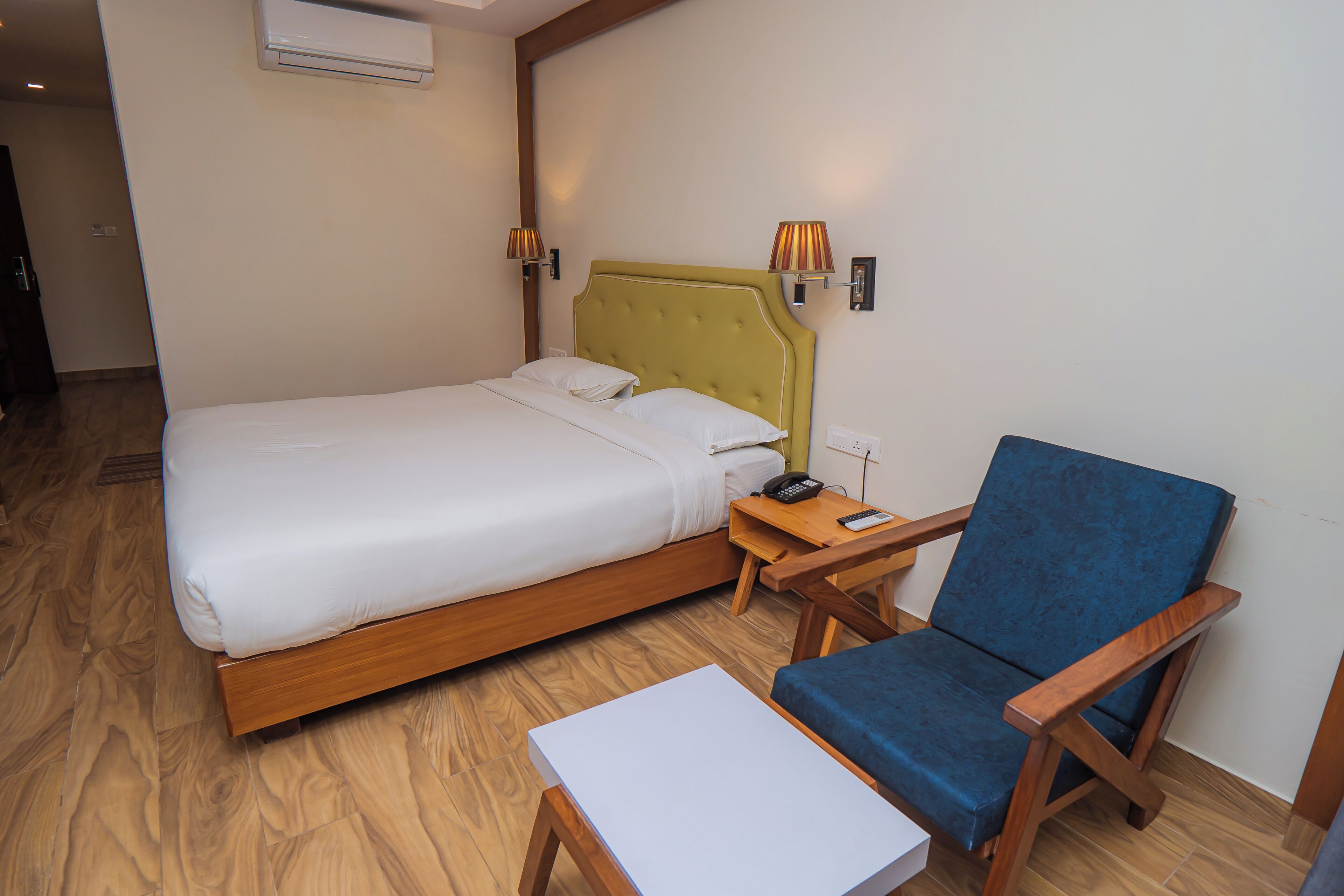 Una habitación de hotel con cama, mesita de noche, silla y aire acondicionado.