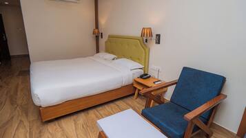 Una habitación de hotel con cama, mesita de noche, silla y aire acondicionado.