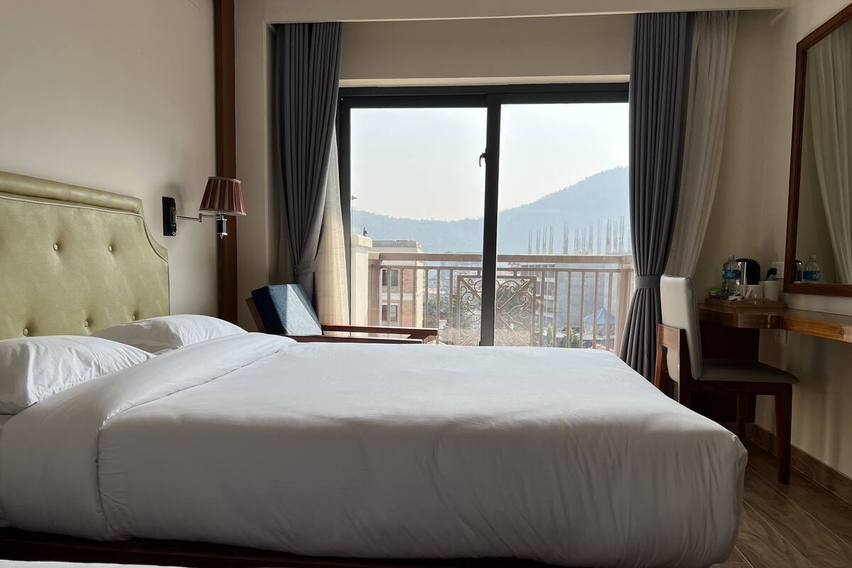 Habitación de hotel con una cama grande, una silla, un escritorio con espejo y vistas a las montañas a través de la ventana.