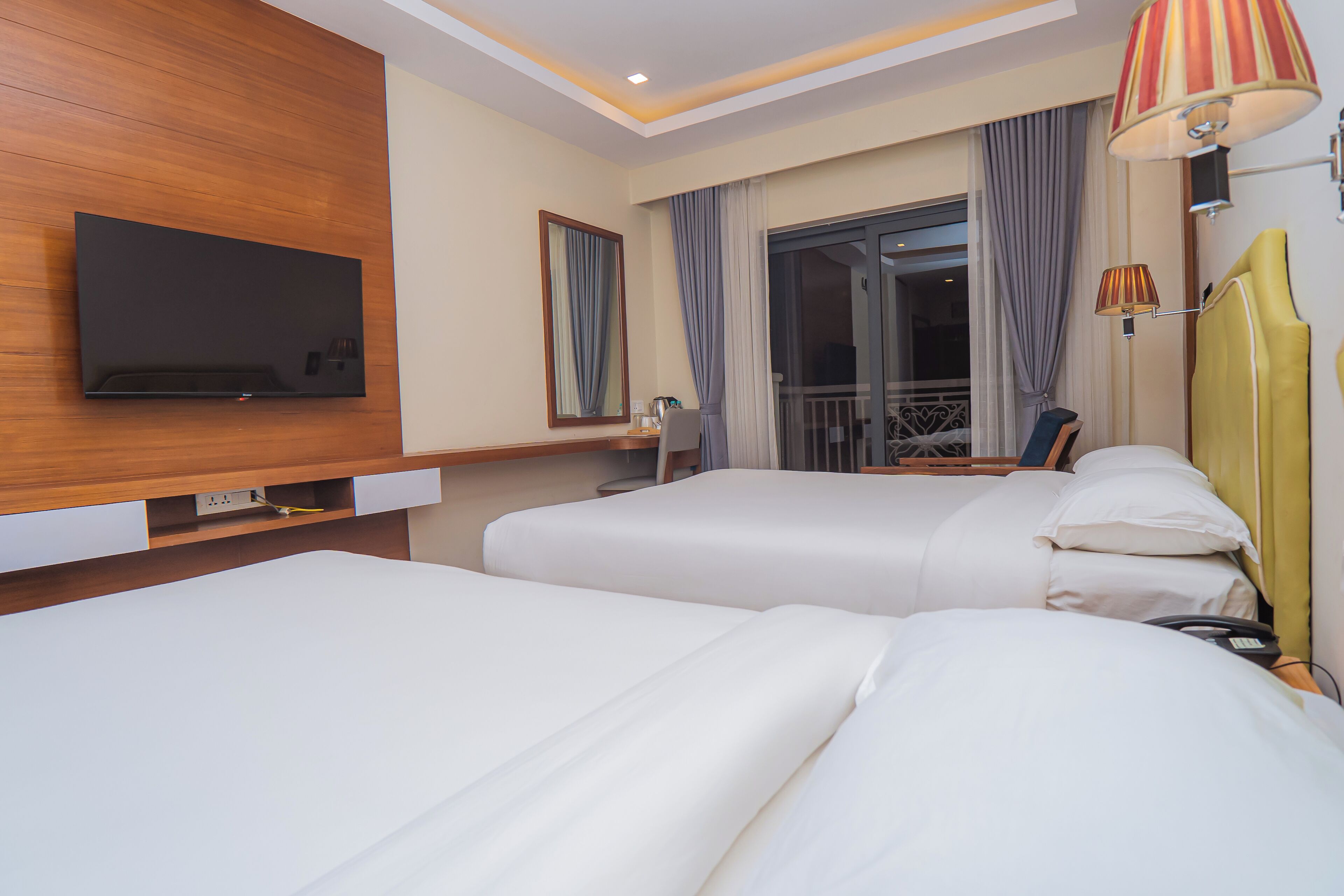 Une chambre d’hôtel avec deux lits, un téléviseur à écran plat fixé au mur, un bureau avec une chaise et une fenêtre avec des rideaux.