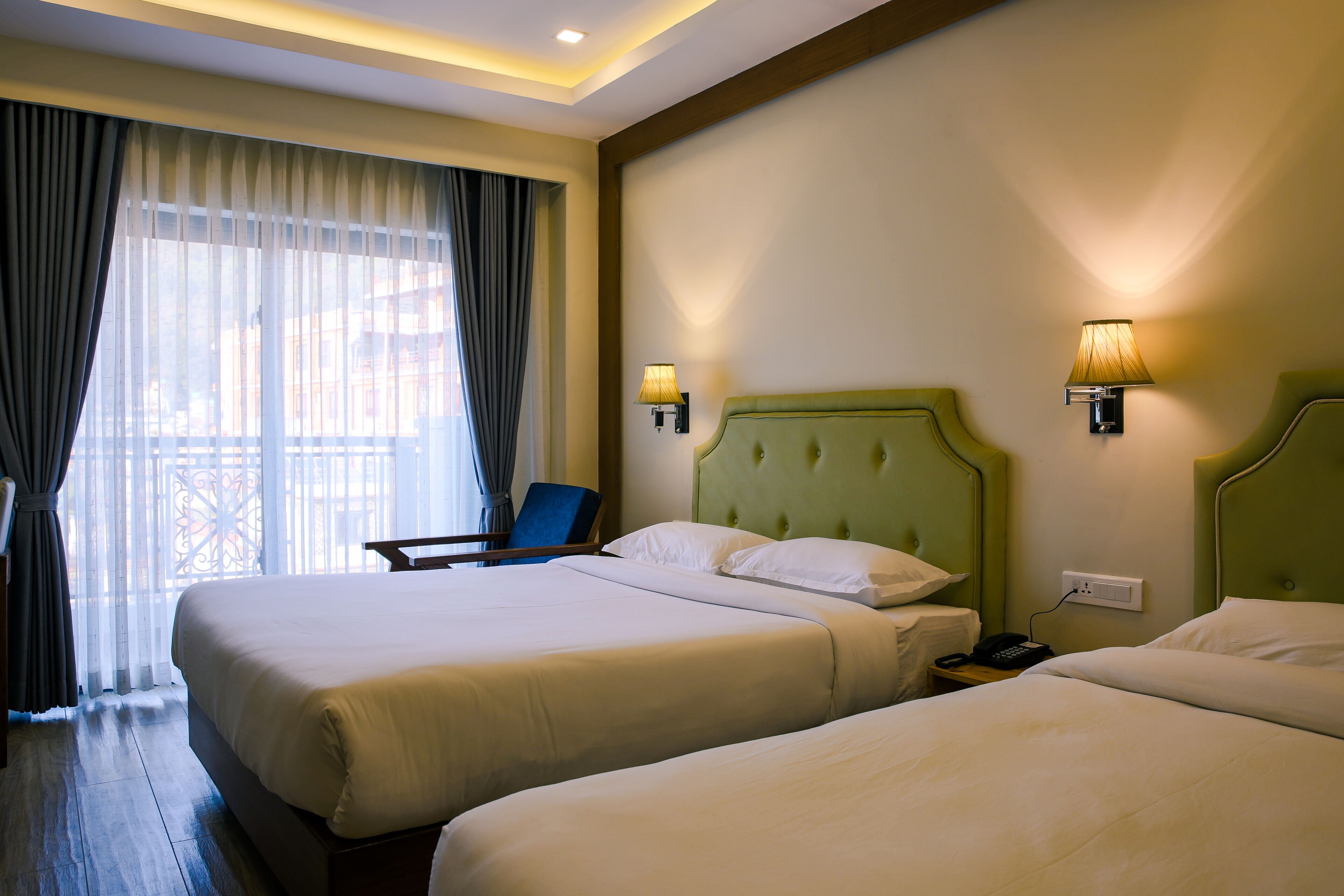 Habitación de hotel con dos camas, una silla, un escritorio con teléfono y una ventana con cortinas.
