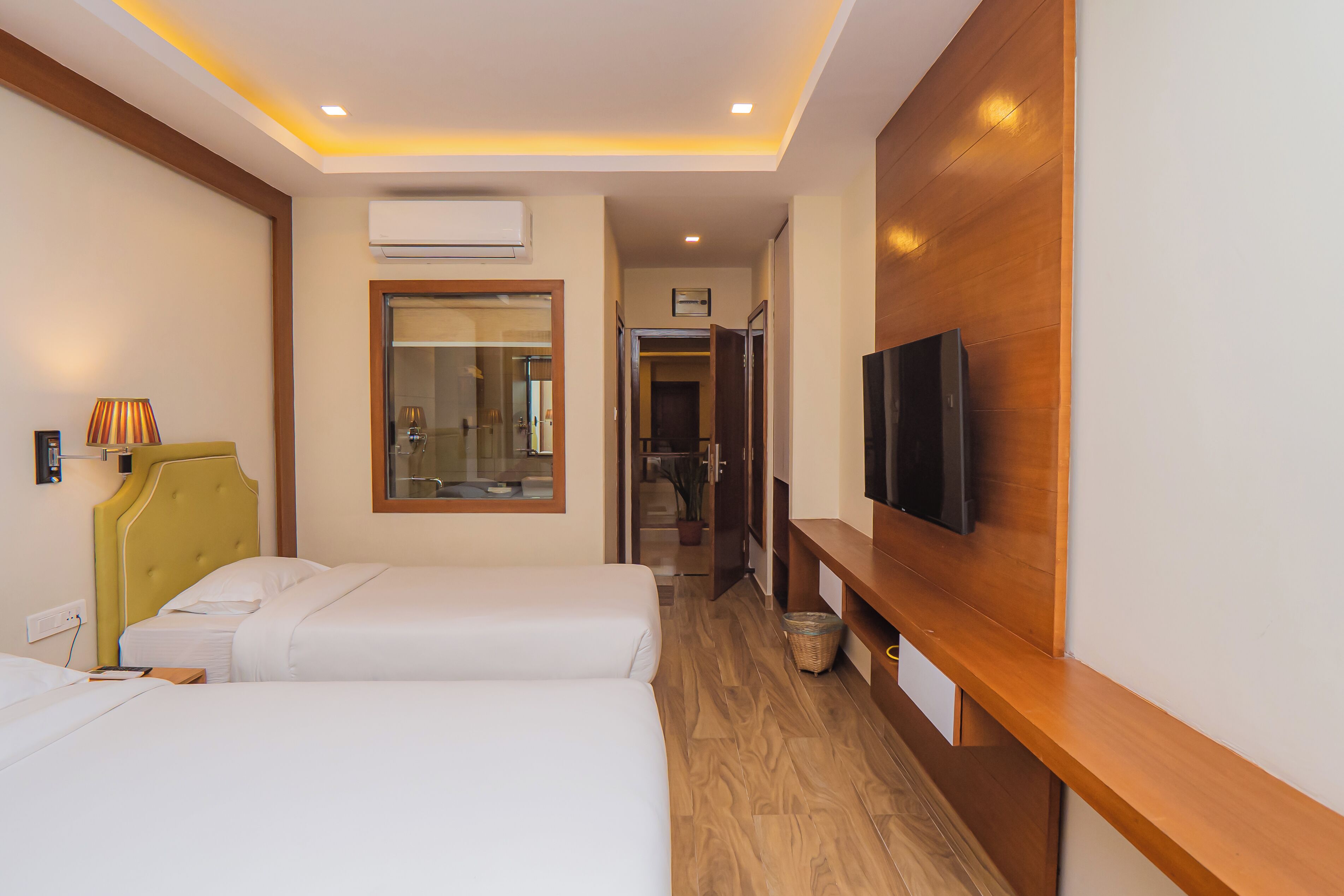 A hotel room with two beds, a television on the wall, and a wooden bench.