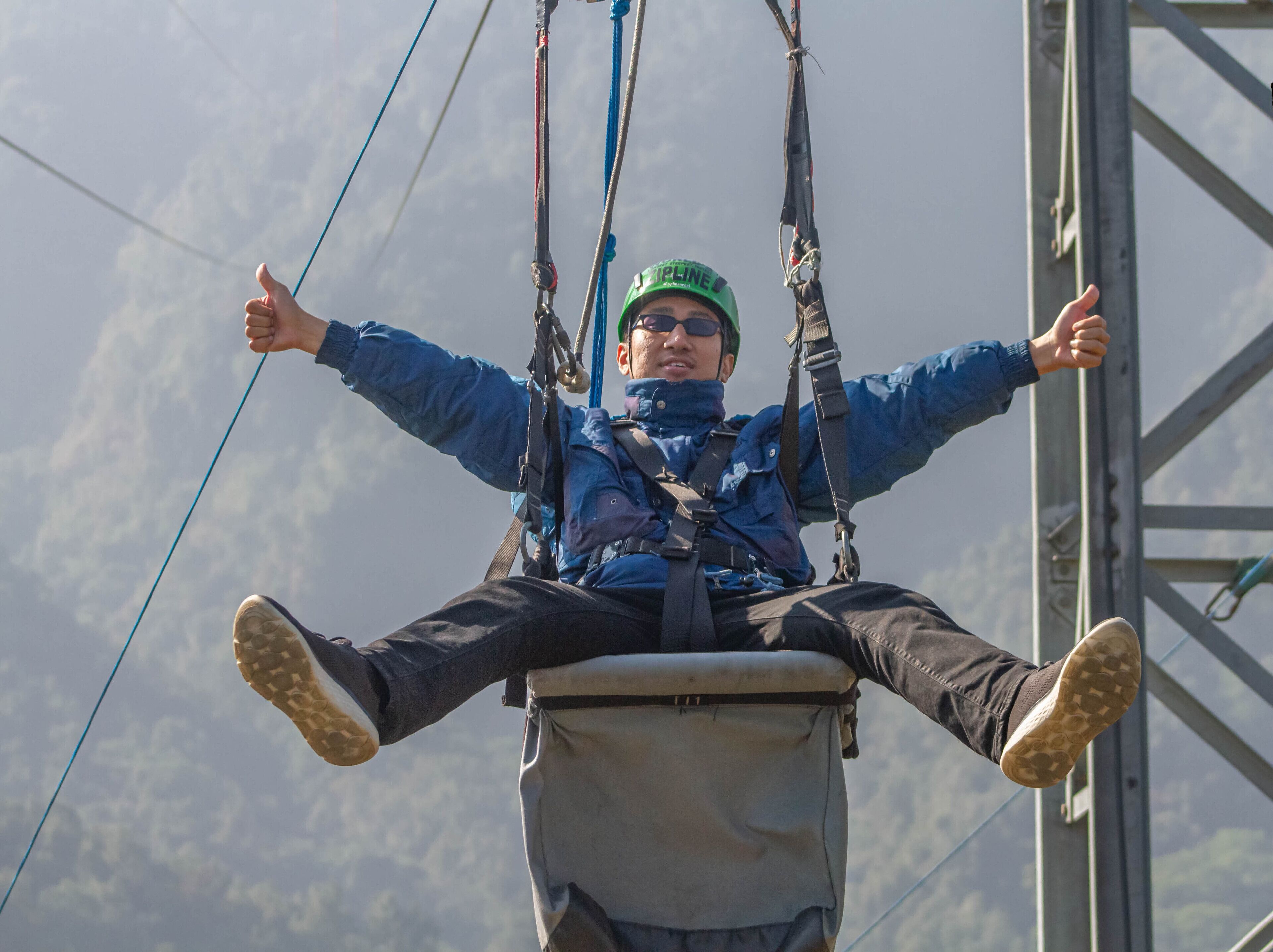 A person suspended in a harness, wearing a helmet and safety gear, with a clear sky in the background.