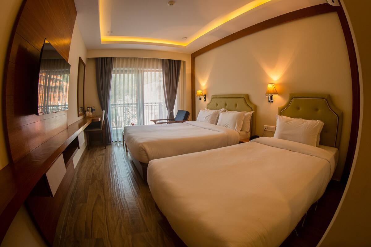 Habitación de hotel con dos camas, un banco de madera, un televisor y vistas al exterior.