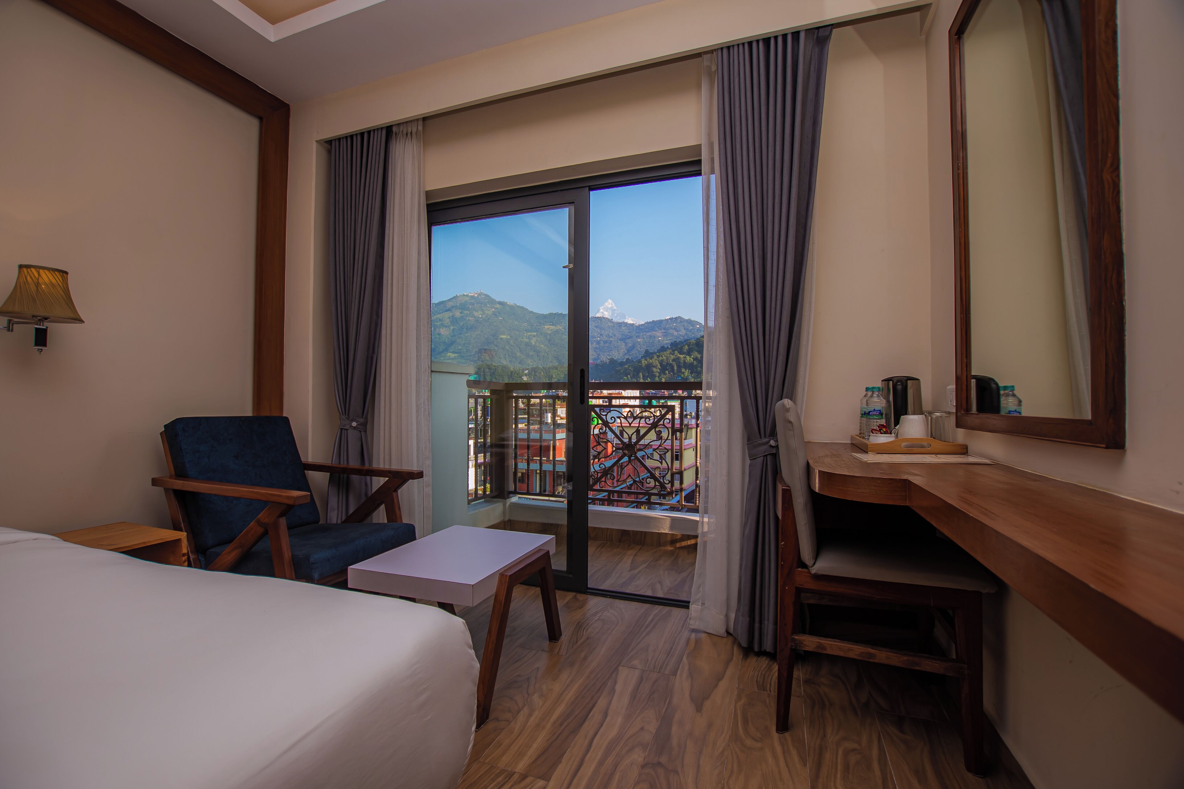 Een hotelkamer met een bed, een bureau, een stoel en een balkon met uitzicht op bergen.