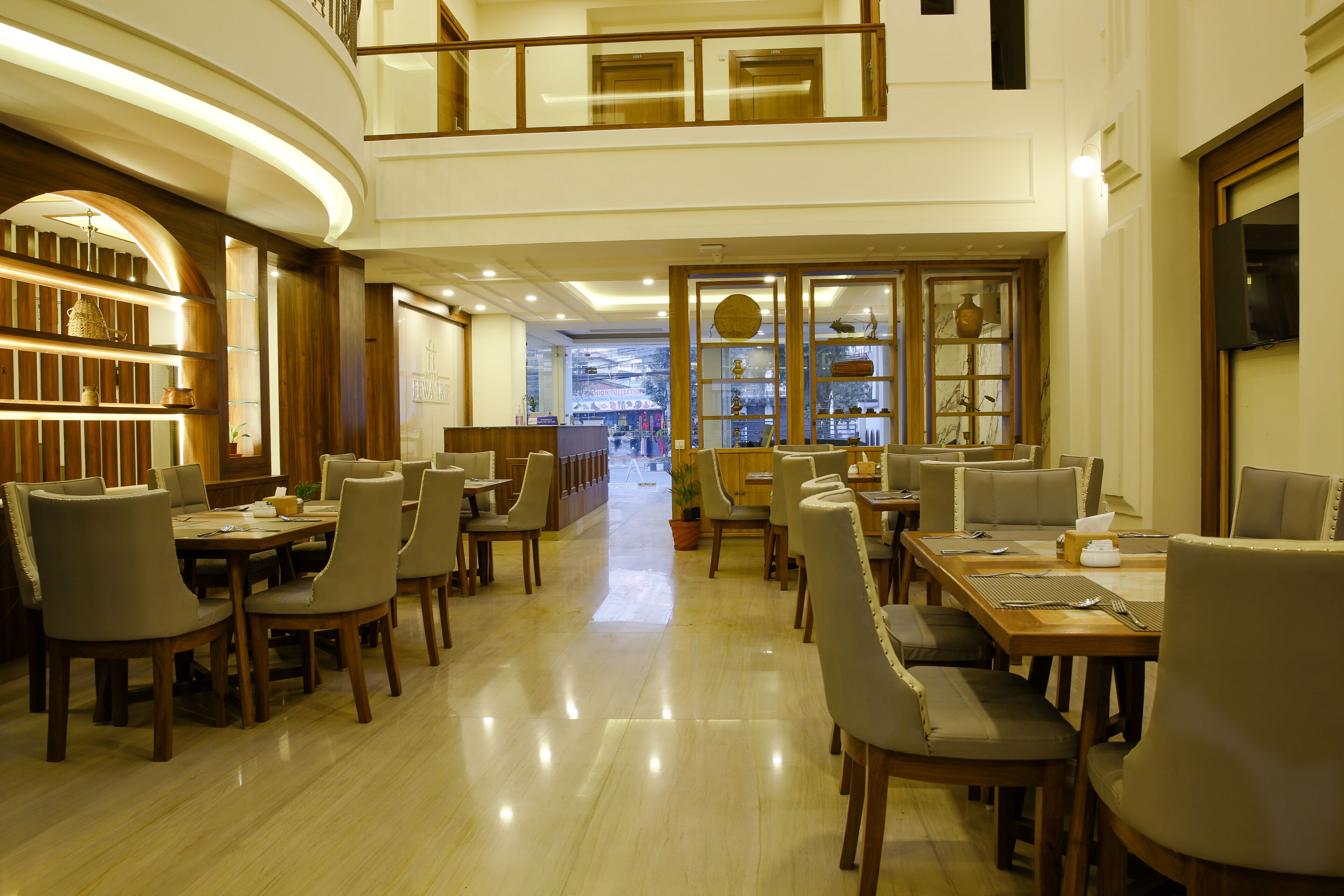 Um amplo saguão de hotel com várias áreas de refeição, um balcão de recepção central e vista para a cidade através de grandes janelas.