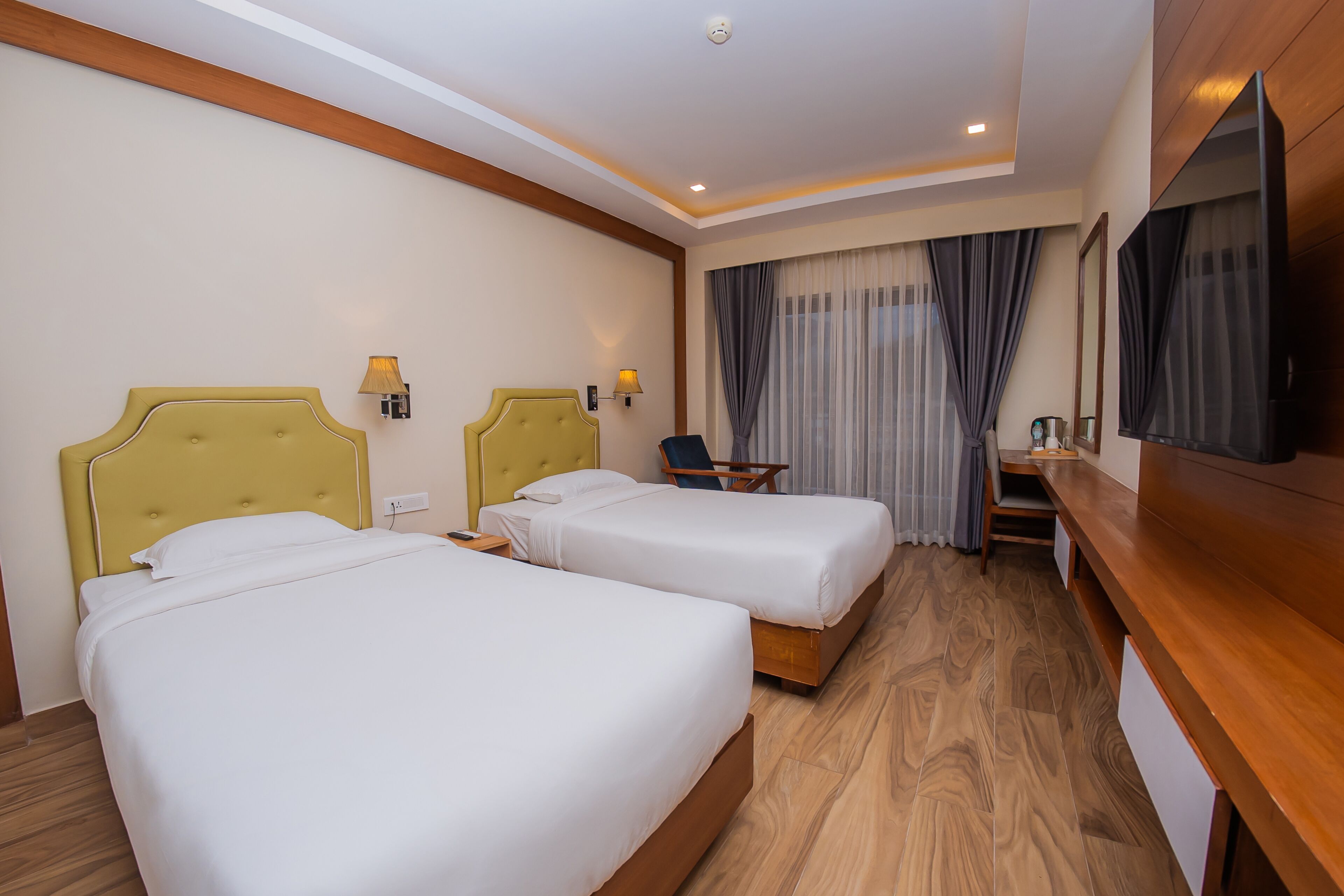 A hotel room with two beds, a desk, a chair, a TV, and a window with curtains.