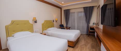 A hotel room with two beds, a desk, a chair, a TV, and a window with curtains.