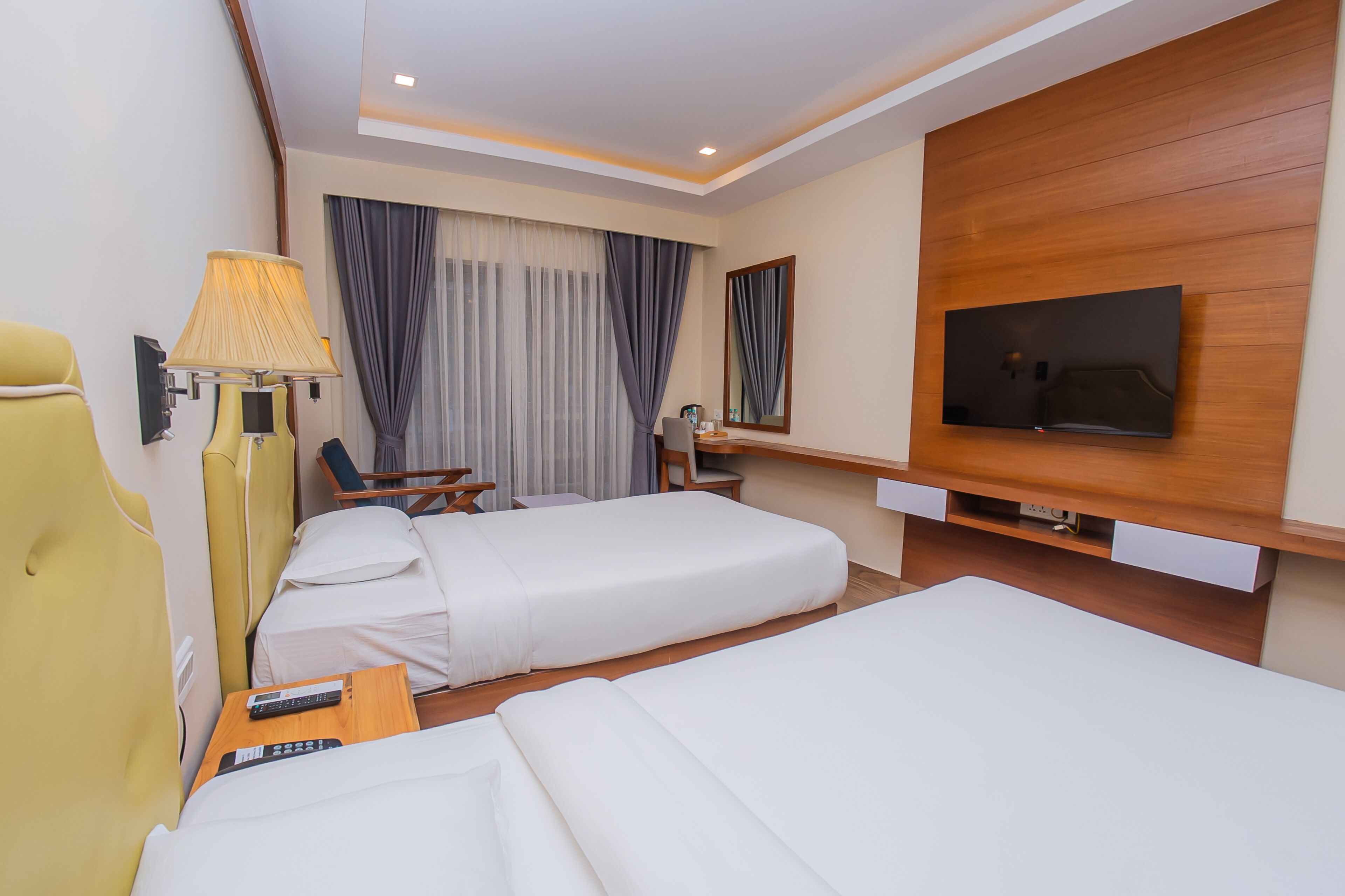 A hotel room with two beds, a TV, a desk, a chair, a lamp, and a window with curtains.