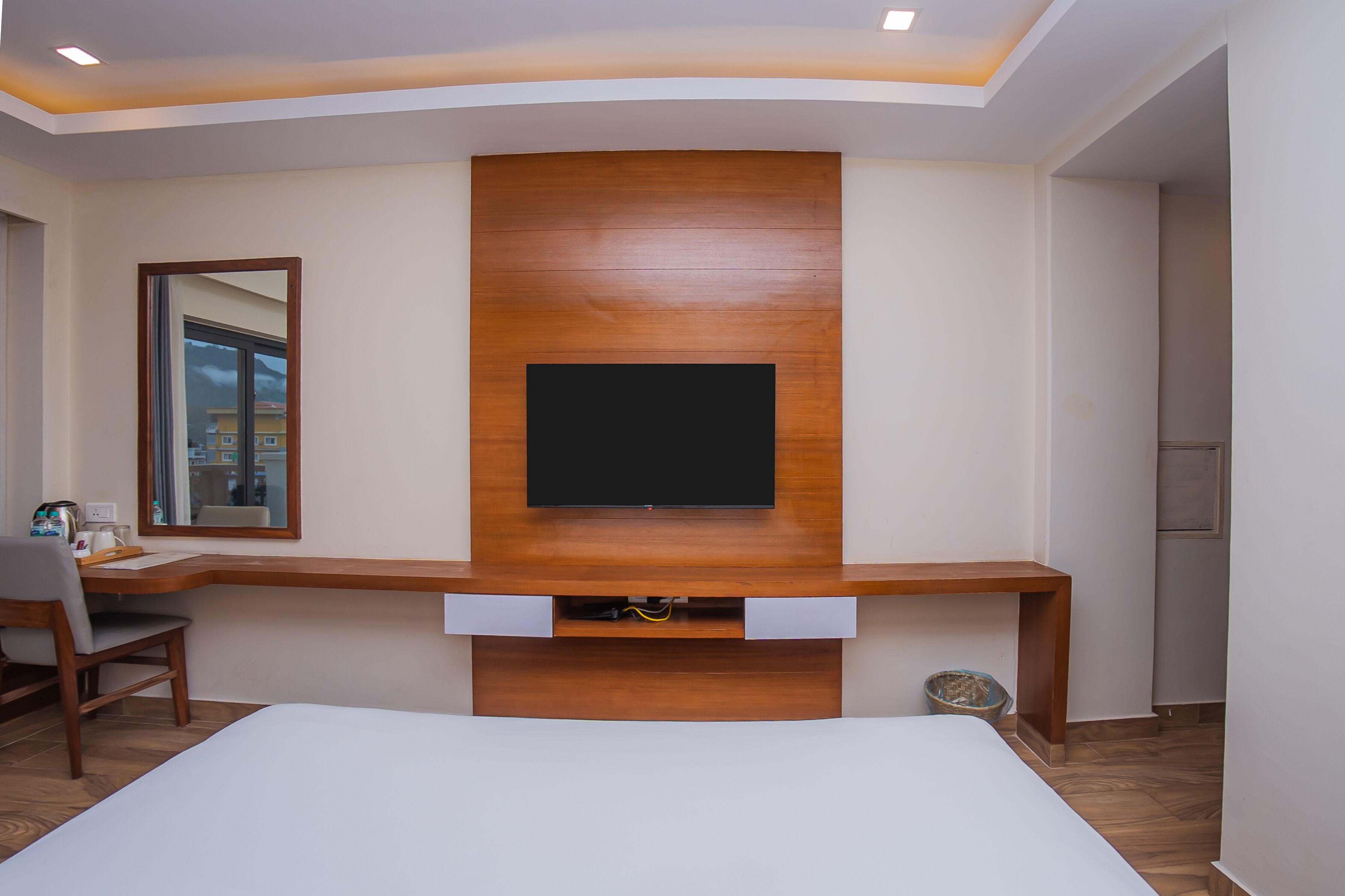 Habitación de hotel con una estantería de madera, un televisor de pantalla plana, un escritorio con una silla y una cama.