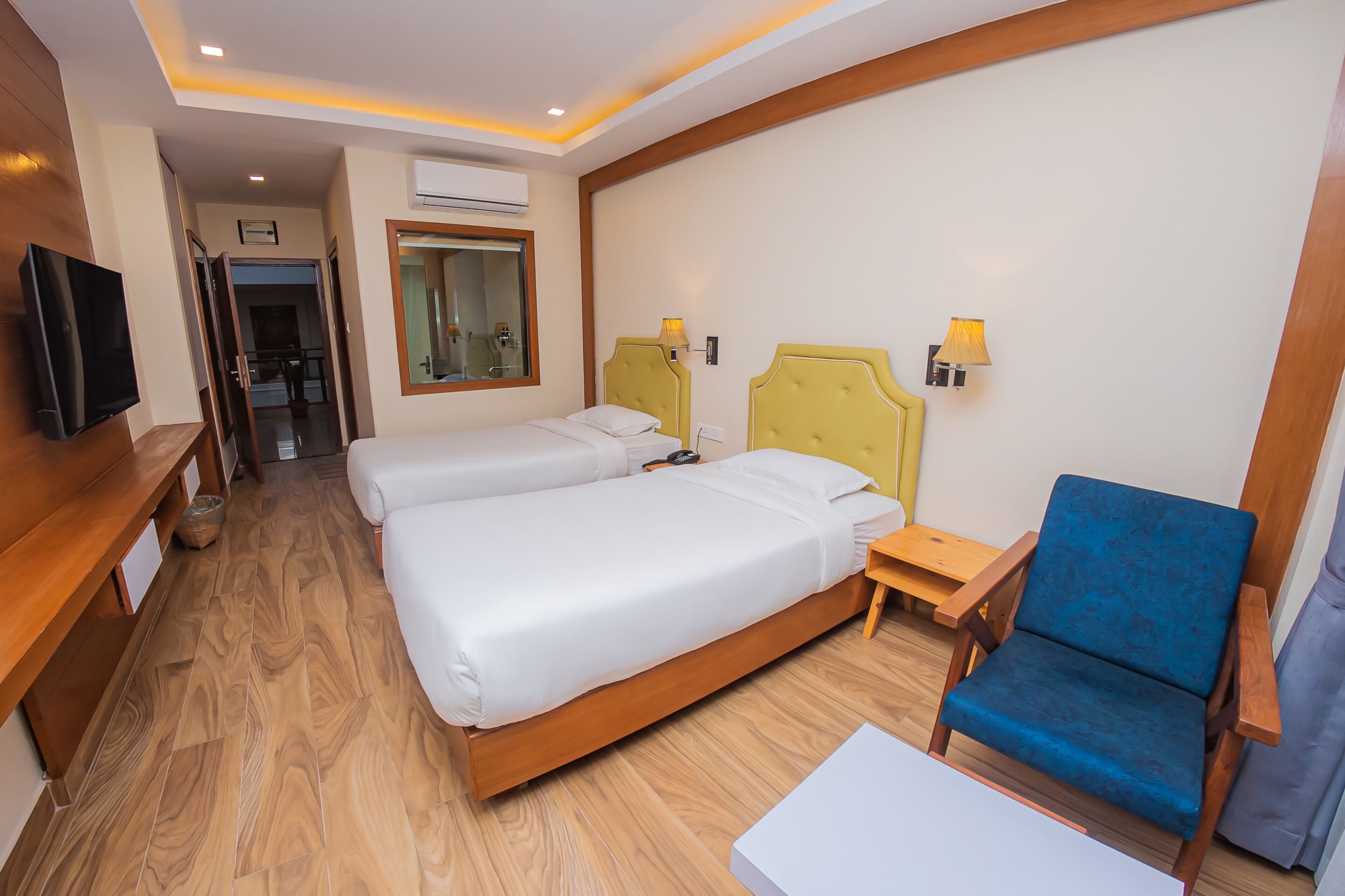 A hotel room with two beds, a TV, a wooden floor, and a blue chair.