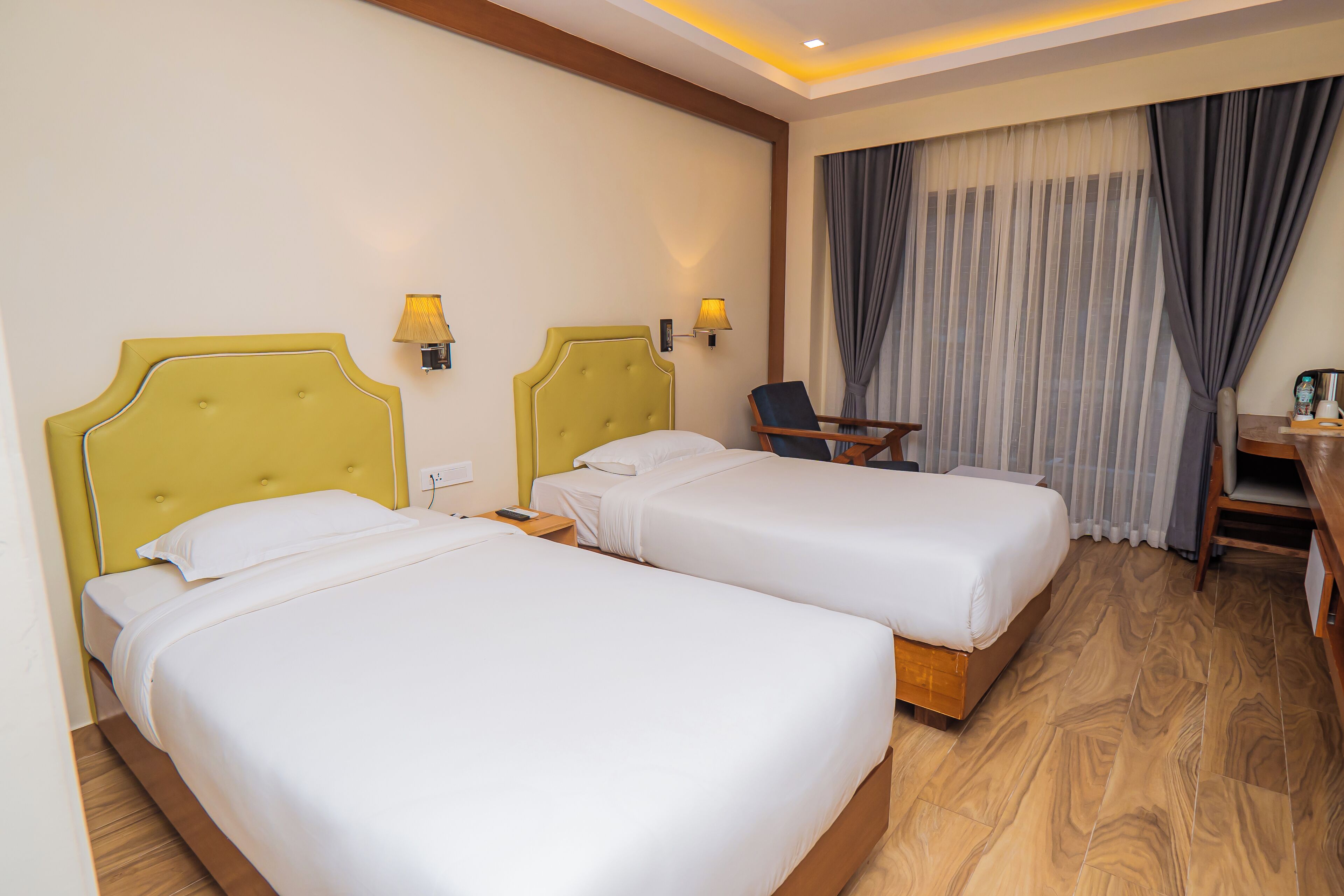 A hotel room with two beds, a desk, a chair, and a window with curtains.