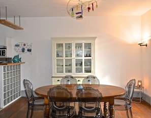 A dining area with a wooden table and chairs, a white cabinet with glass doors, and a hanging light fixture.