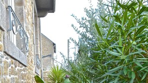 A narrow brick pathway flanked by lush green plants and a stone building with a metal railing. - Ker Lucienne" 50m from the "sillon" beach in the center of town, 12 minutes from the city center and the TGV train station. (Saint-Malo)