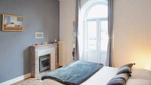 A bedroom with a fireplace, a large window with curtains, and a bed with pillows. - Ker Lucienne" 50m from the "sillon" beach in the center of town, 12 minutes from the city center and the TGV train station. (Saint-Malo)